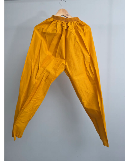 Mustard yellow pants hanging on a hanger against a plain background