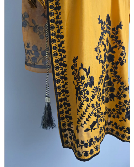 Yellow fabric with black floral embroidery and a tassel on a light blue background